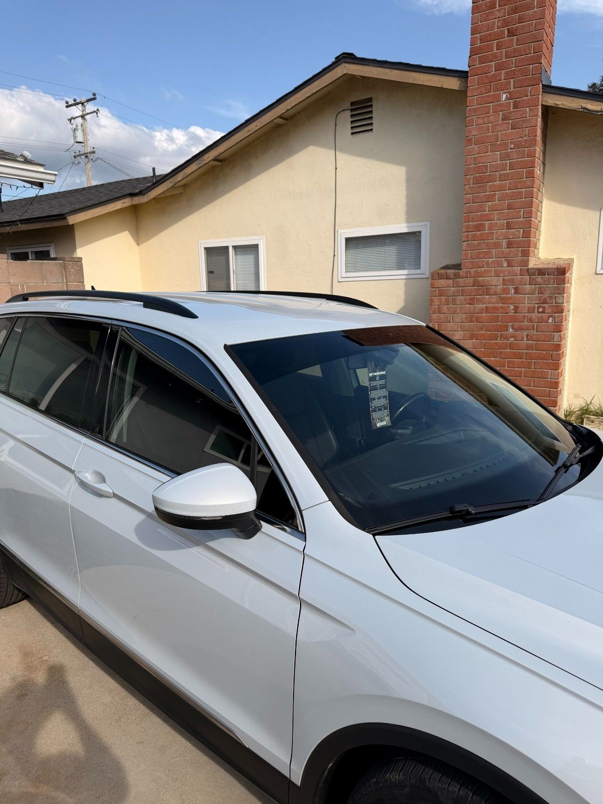 A white SUV parked in a driveway in front of a house with a brick chimney under a clear blue sky.