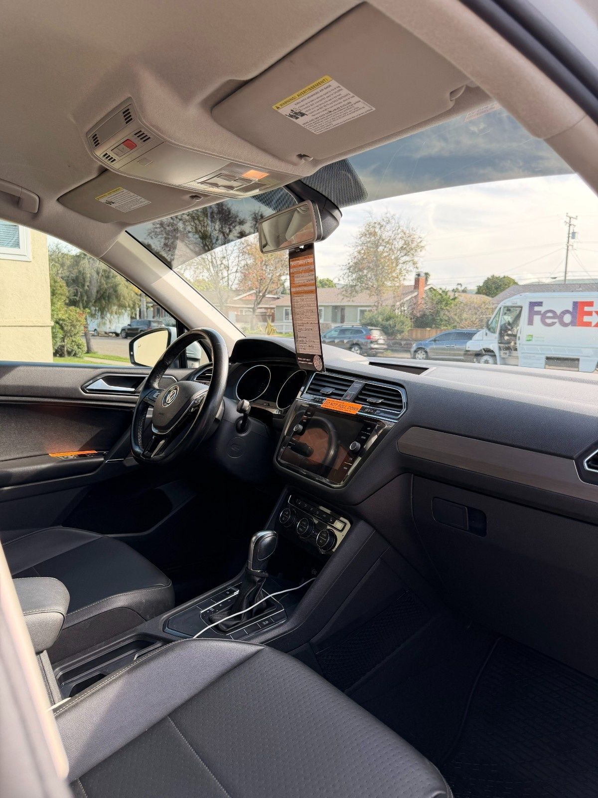Interior view of a modern car from the driver's seat, showing the steering wheel, dashboard, and a view of a street.