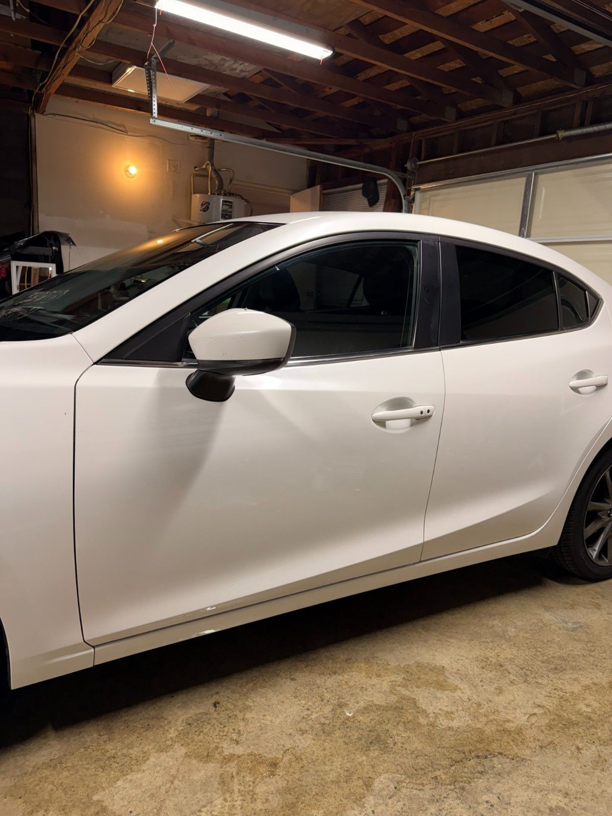 A white sedan parked inside a garage with its side profile visible.