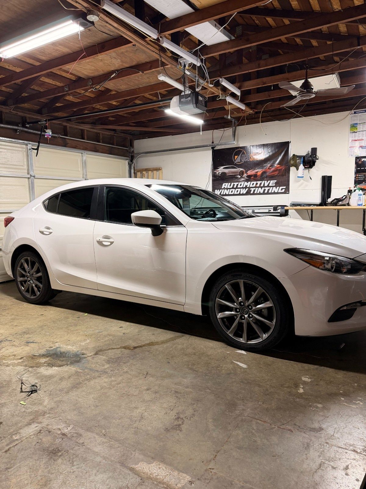 White sedan parked inside a garage with exposed wooden ceiling beams and a hanging banner.