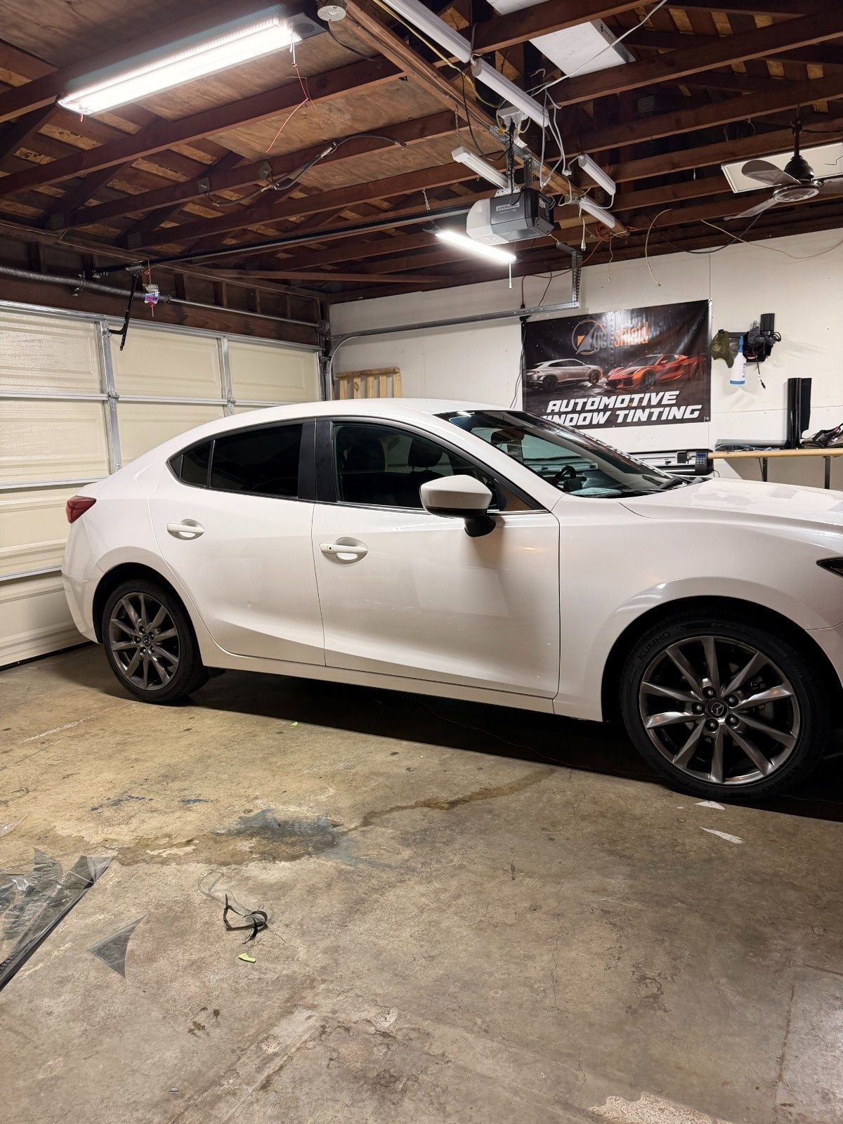 A white sedan parked inside a garage with overhead lighting and a banner on the wall.