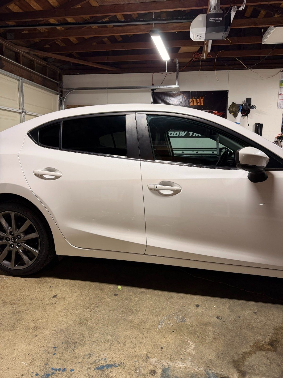 Side view of a white sedan parked inside a garage with wooden ceiling beams and a hanging light fixture.