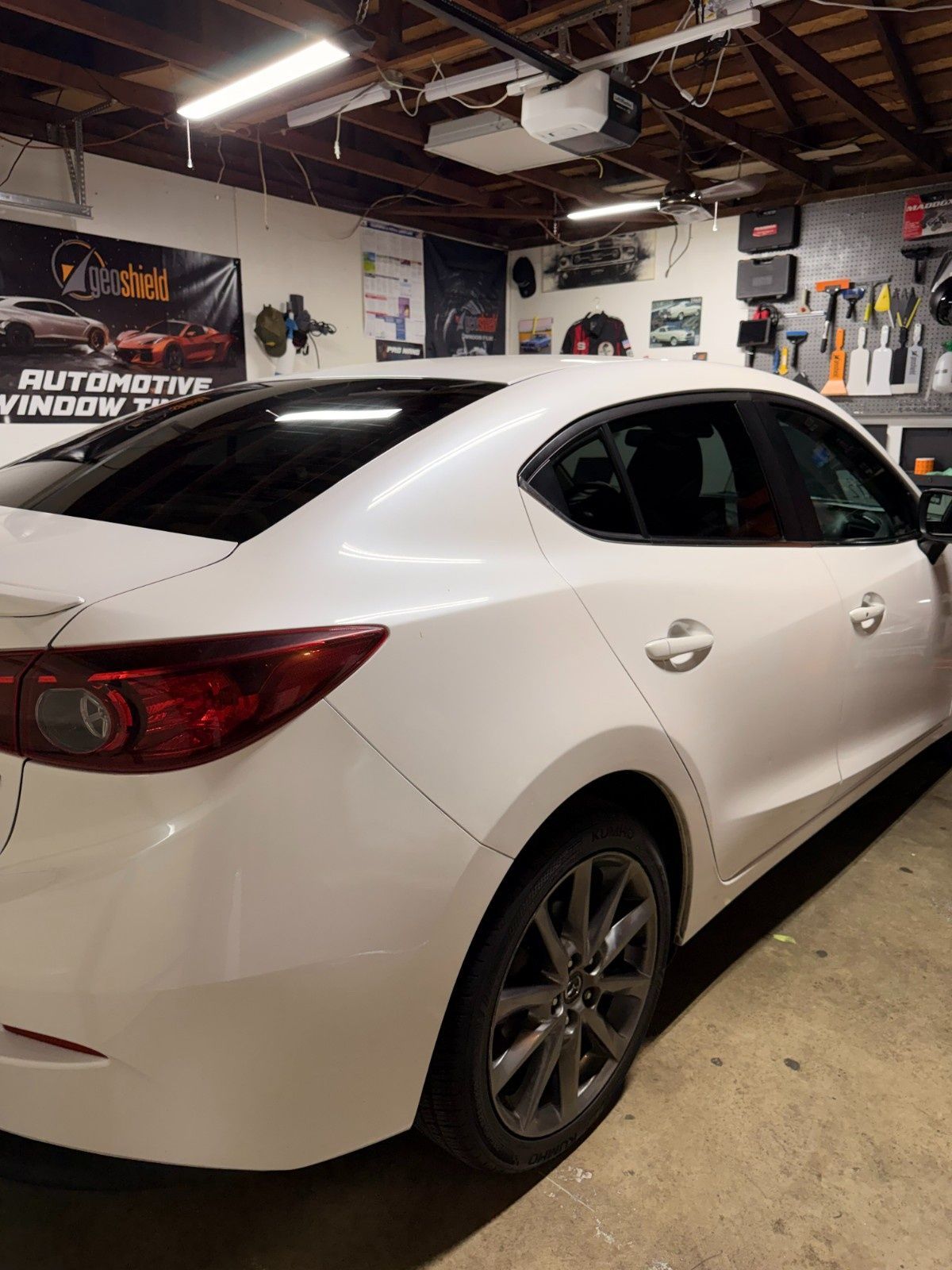 A white sedan parked in a well-lit garage, viewed from the rear passenger side.