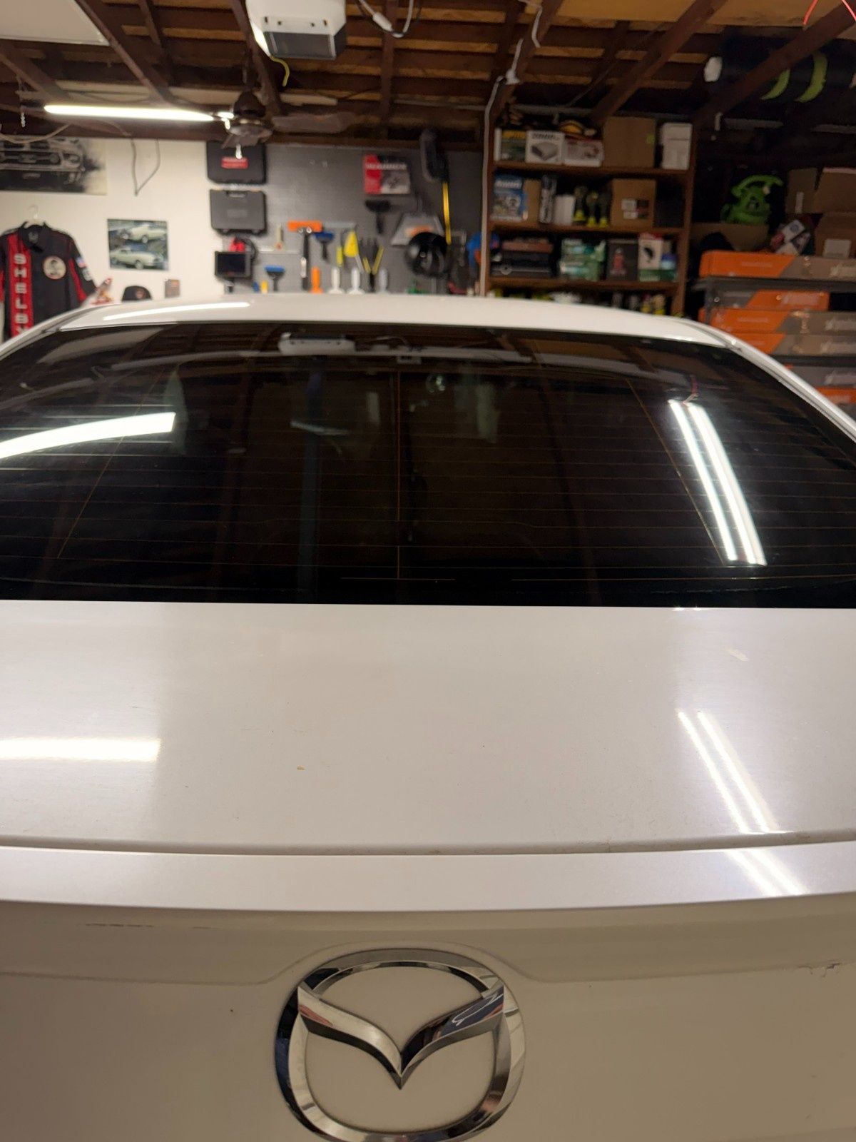 The rear view of a white Mazda sedan parked inside a garage with shelves of supplies in the background.