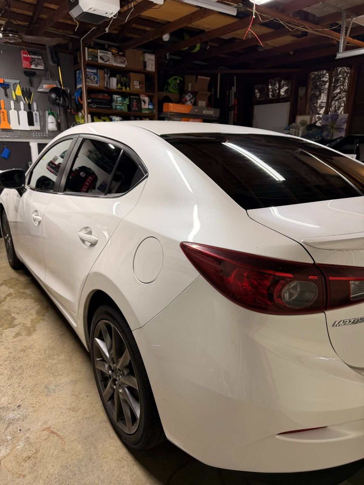 A white Mazda 3 sedan parked inside a residential garage, viewed from the rear passenger side angle.