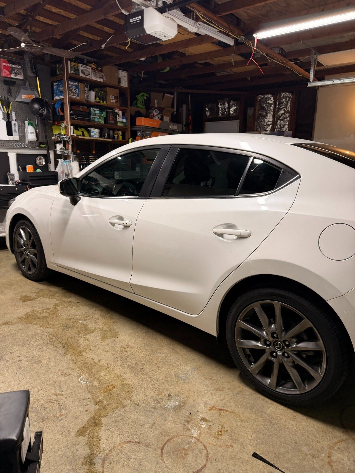 A white sedan parked inside a garage with shelves of supplies in the background.
