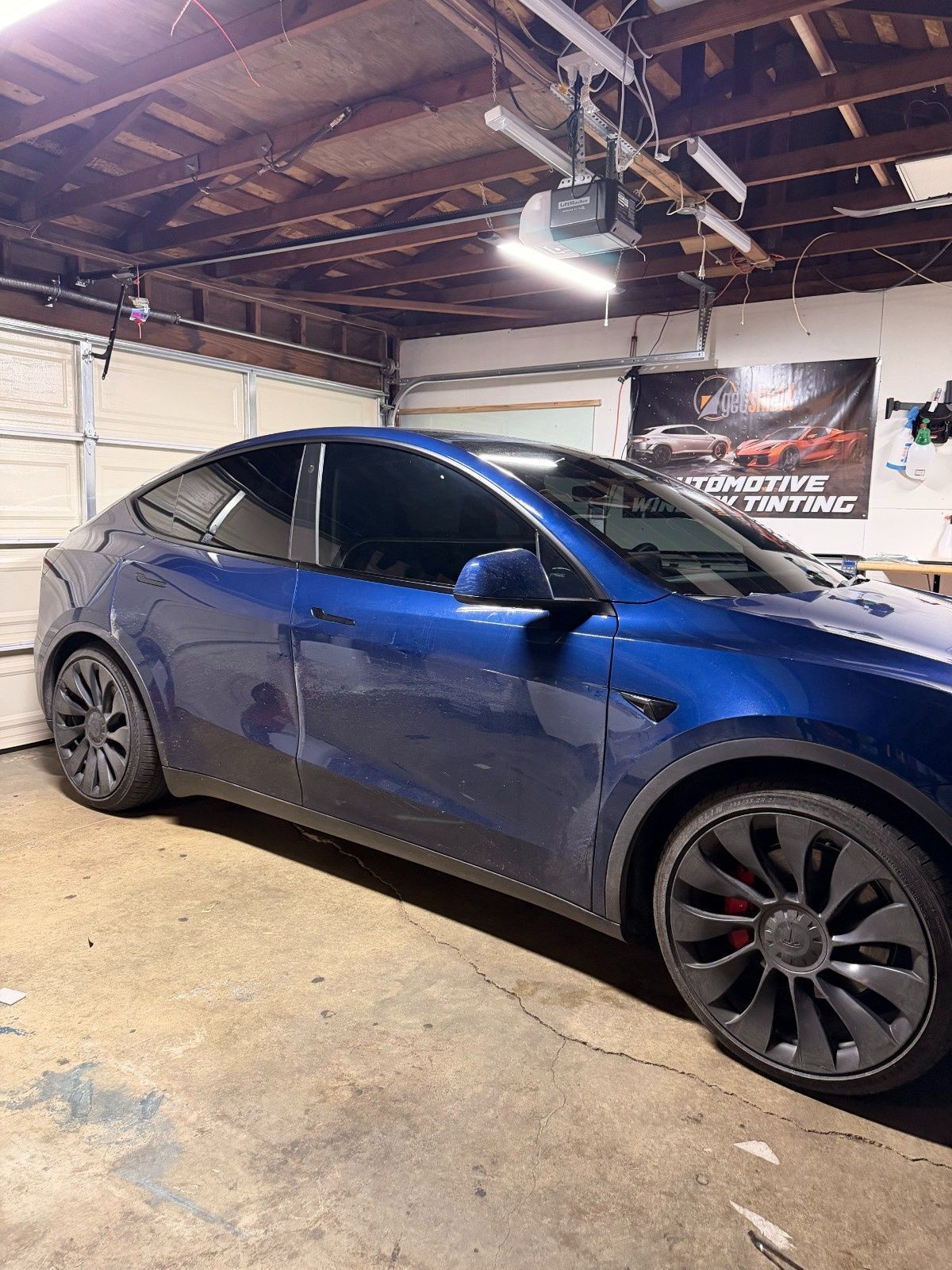 A blue Tesla parked in a garage with large gray wheels and dark tinted windows.