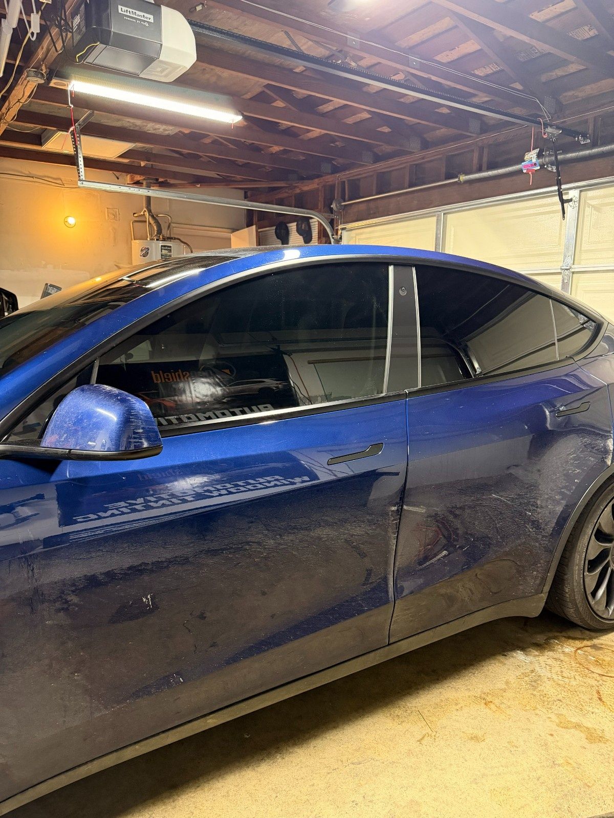 A dark blue Tesla parked inside a residential garage with overhead lighting.