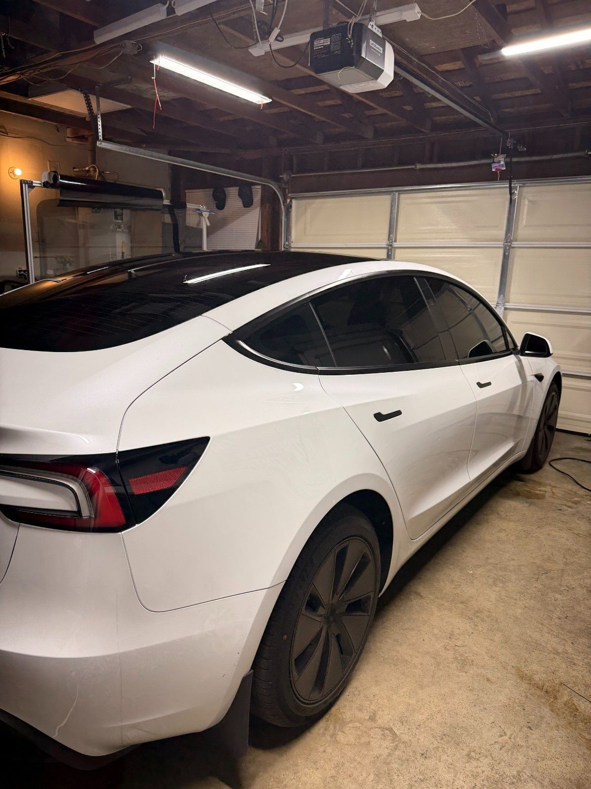 A white Tesla Model 3 parked in a residential garage with black wheels and tinted windows.