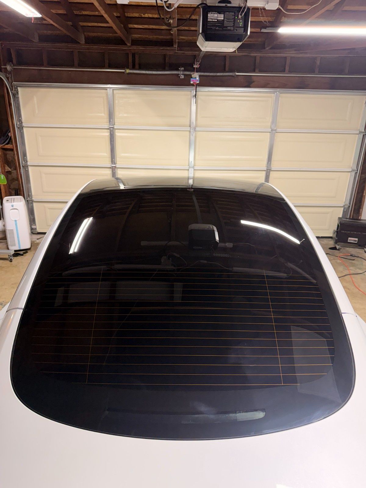 High-angle view of a white car’s dark-tinted rear windshield and glass roof inside a garage with a white sectional door.