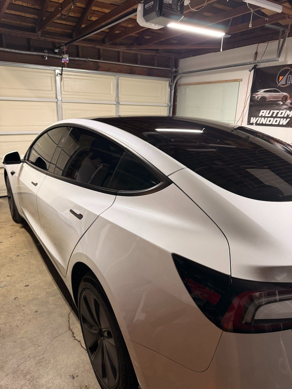 White Tesla Model 3 with tinted windows and black wheels parked inside a garage.