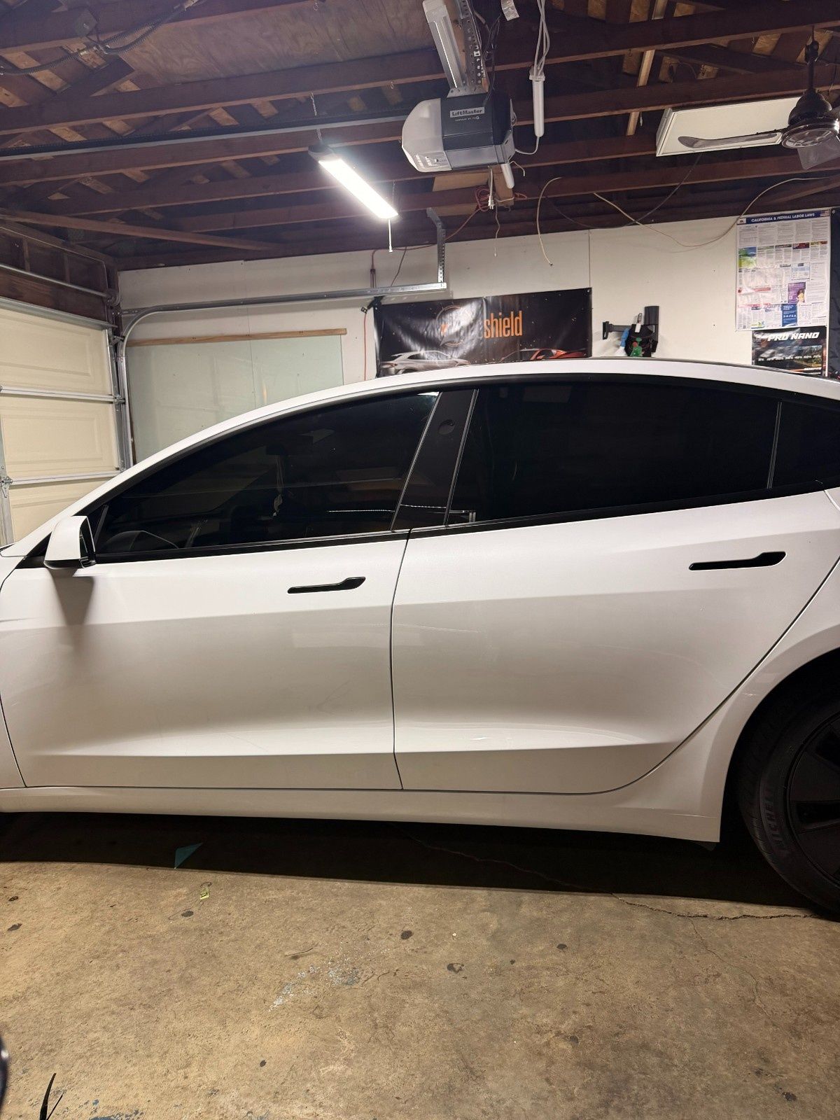 A white Tesla parked inside a garage with black window tint, black door handles, and black wheel covers.