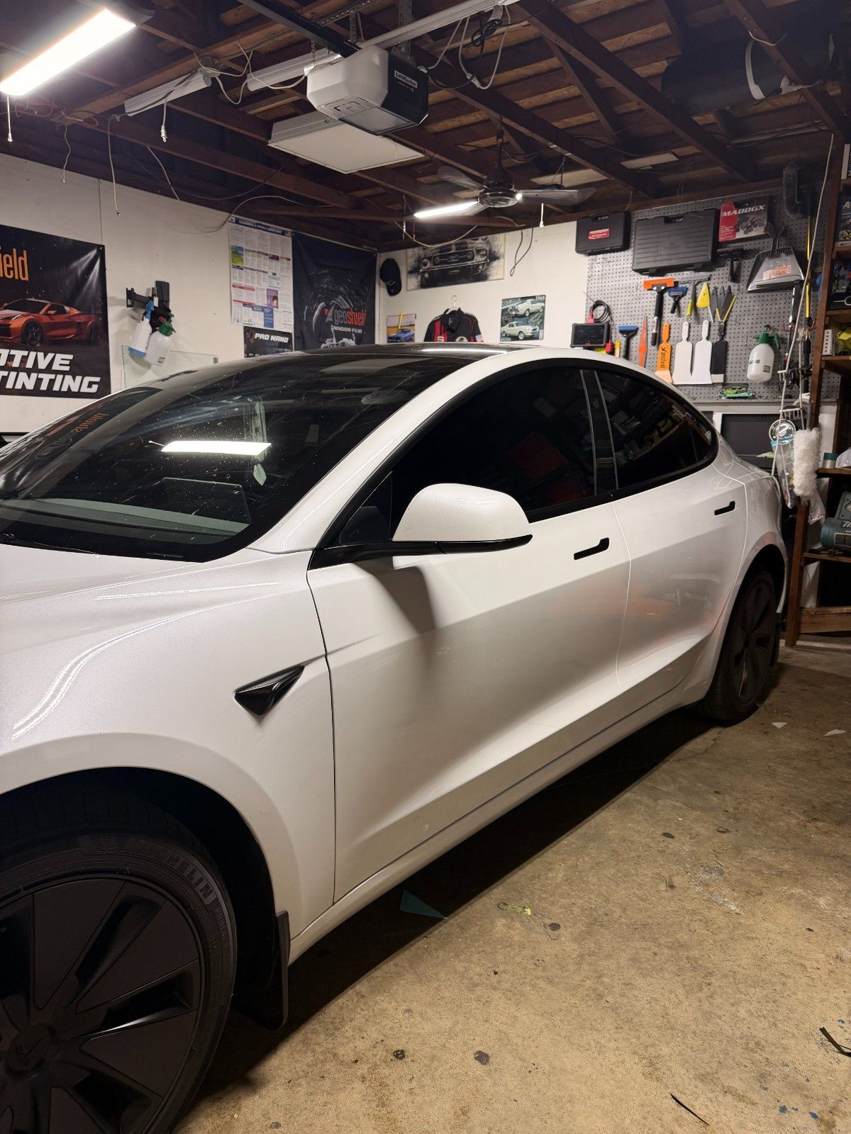 A white Tesla sedan with black wheels and tinted windows parked in a cluttered garage.