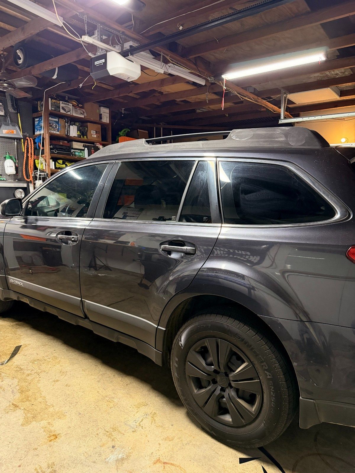 A dark gray SUV parked inside a residential garage with clutter on shelves in the background.