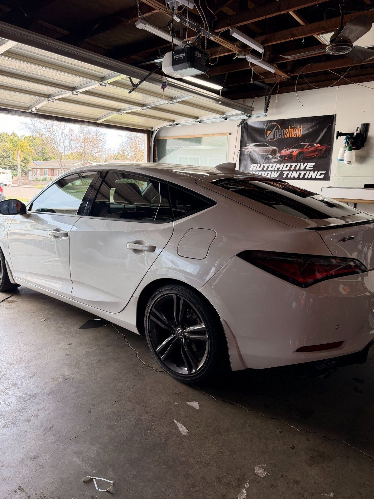 A white Hyundai sedan with tinted windows and dark rims parked inside a garage with a banner in the background.