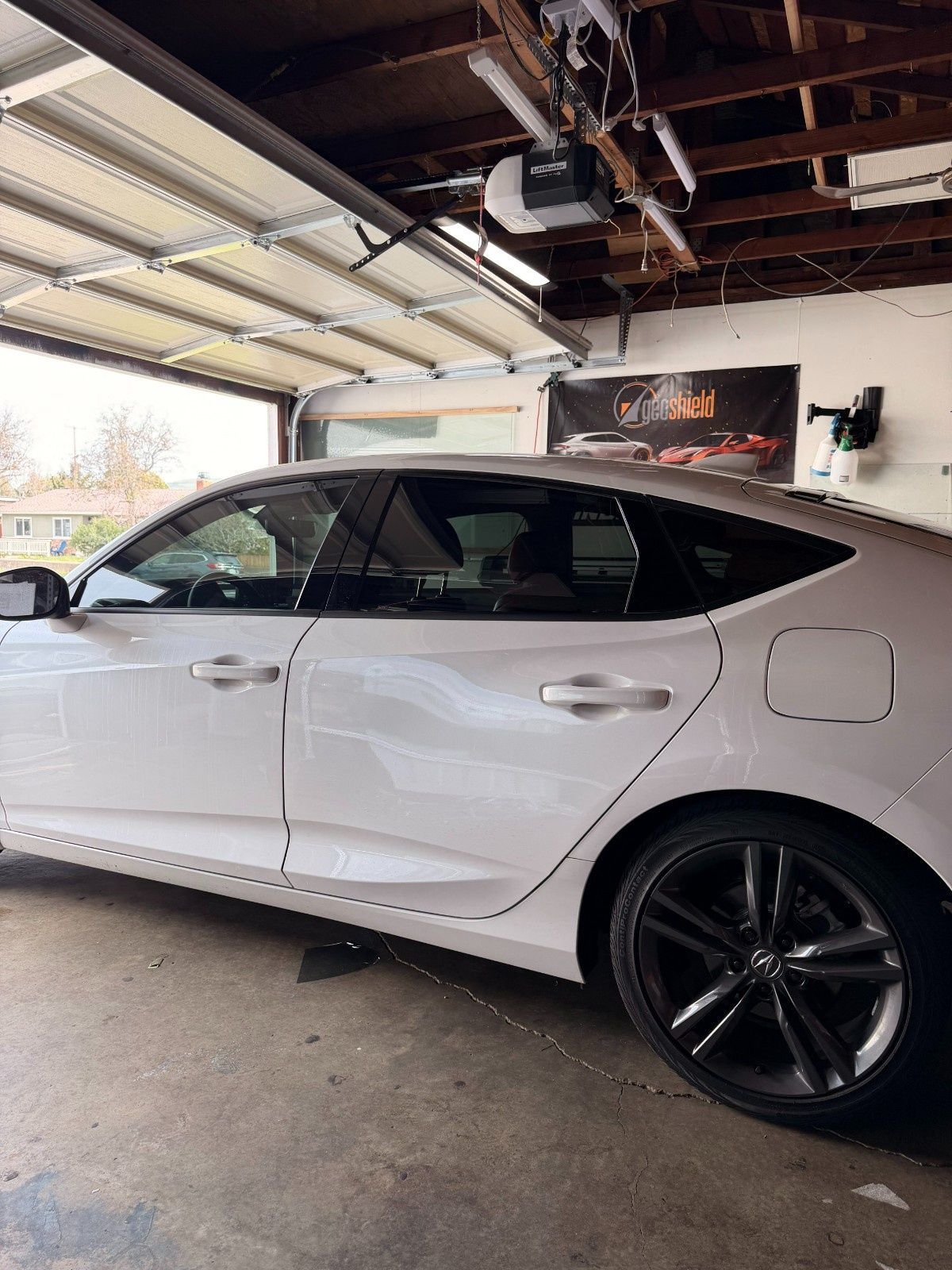 A white sedan parked inside a garage, viewed from the side with the garage door open in the background.