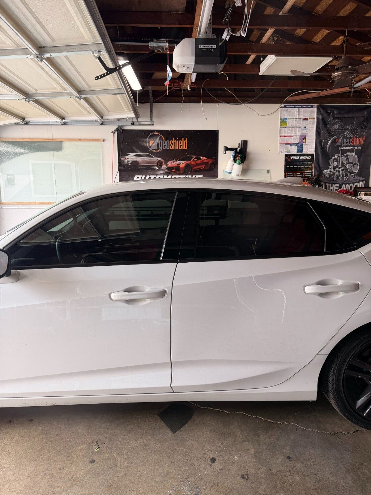 A white sedan parked inside a garage, showing a visible dent on the rear passenger door.