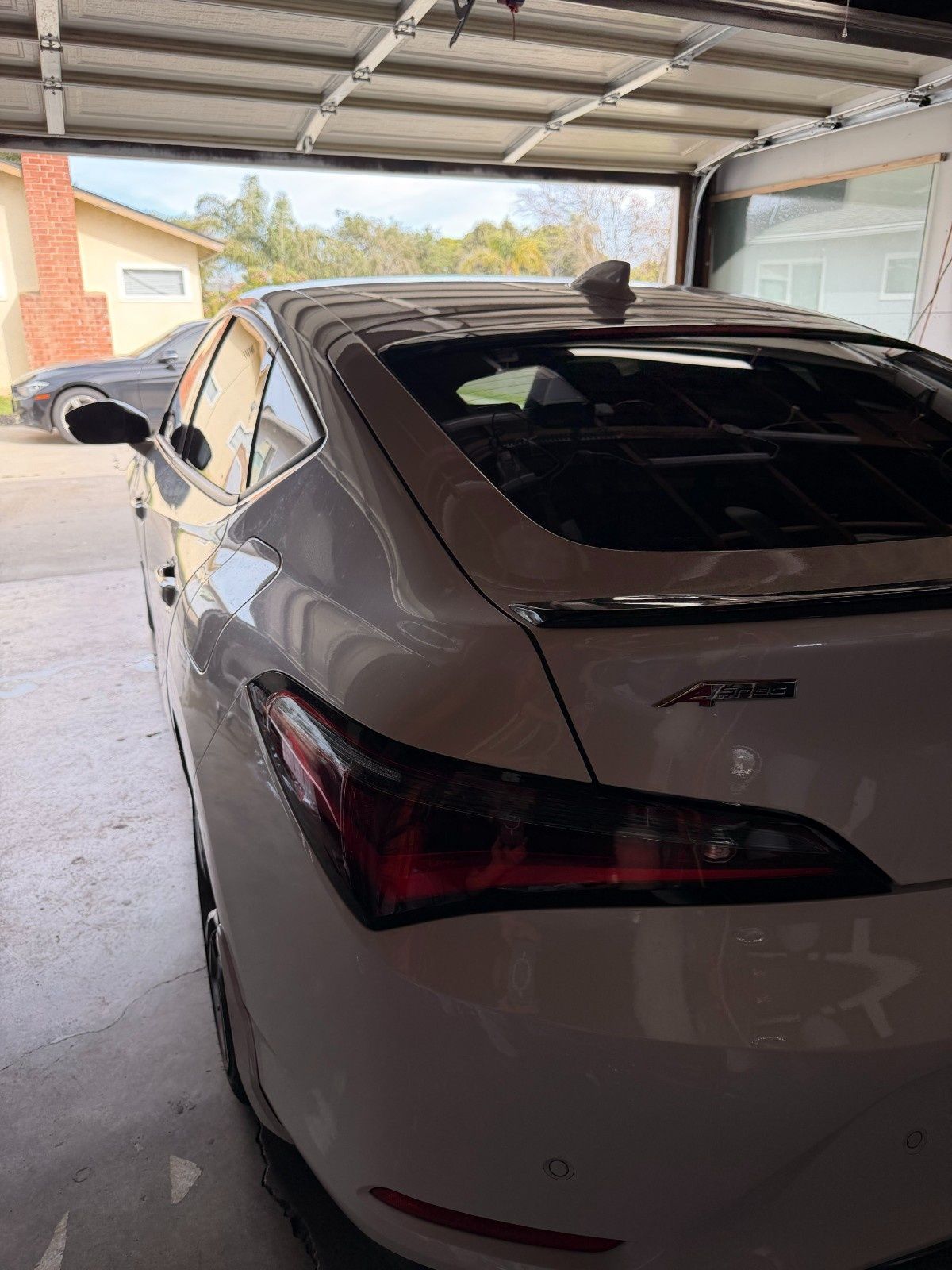 A white Acura sedan with a black spoiler is parked inside a garage, viewed from the rear three-quarter angle.