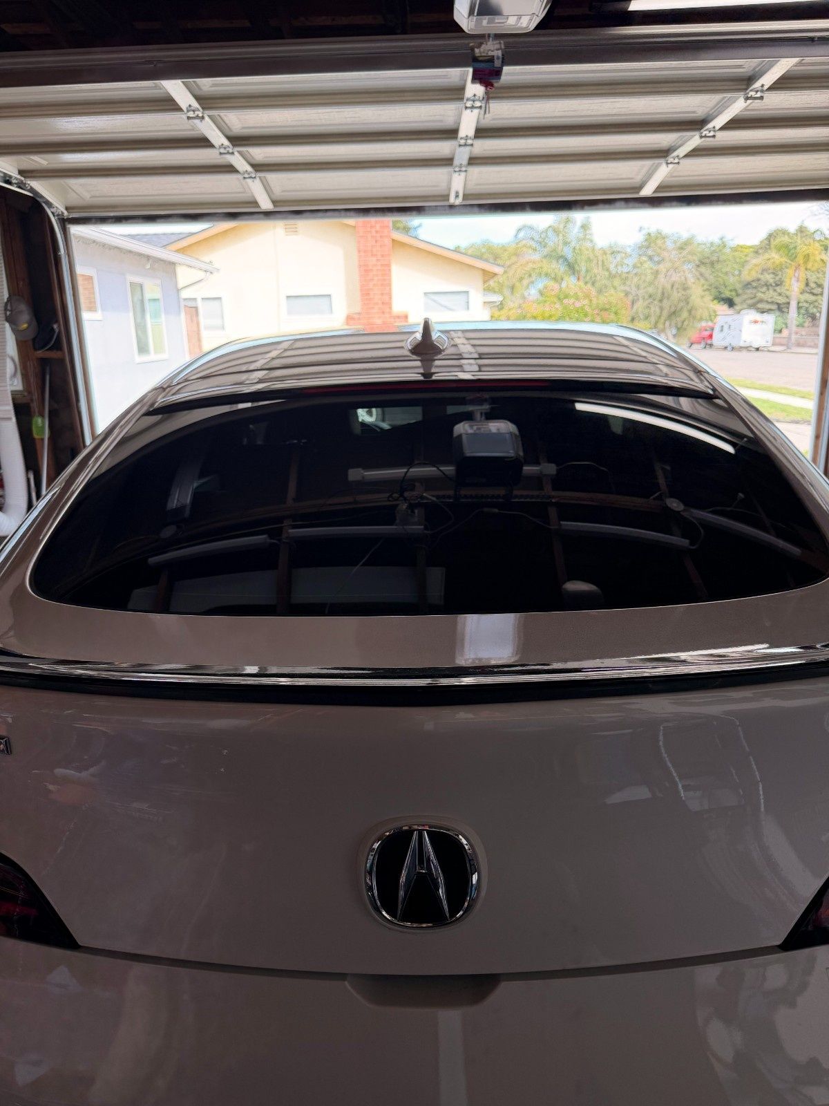 Rear view of a white Acura parked inside a garage, showing the emblem, spoiler, and rear window.