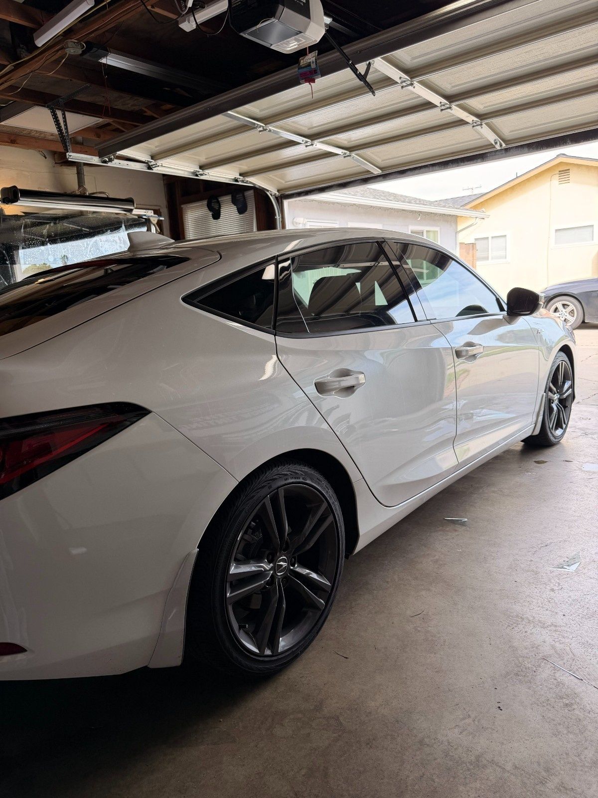 A white sedan parked inside a garage, angled to show its rear quarter, dark alloy wheels, and tinted windows.