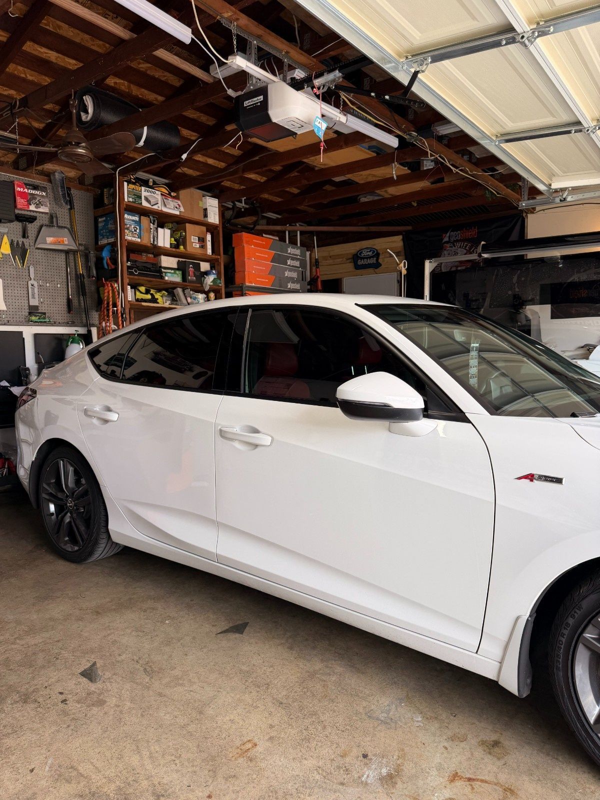 A white sedan with black wheels parked inside a cluttered residential garage.