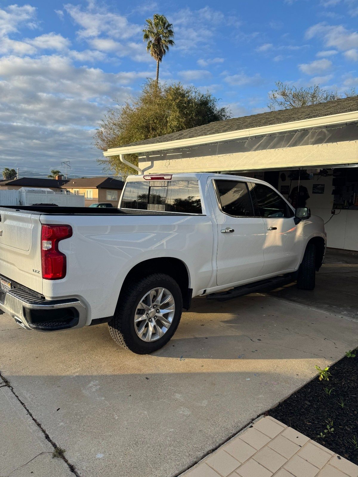 A white Chevrolet Silverado pickup truck parked in a residential driveway under a blue, cloudy sky.