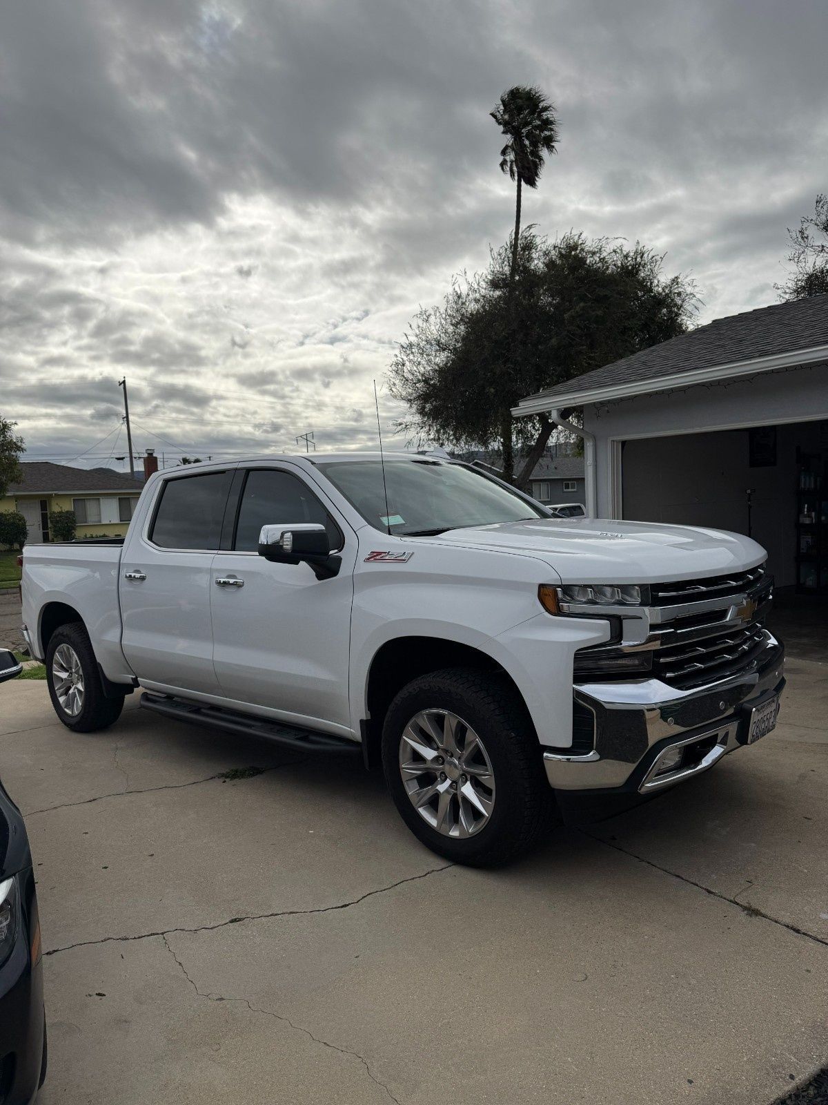 A white Chevrolet Silverado pickup truck parked in a residential driveway under a cloudy sky.