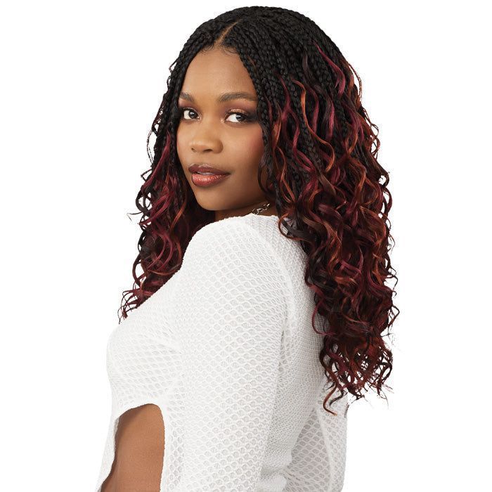 Woman with braided black and red curly hair, wearing a white textured top, looking over her shoulder.
