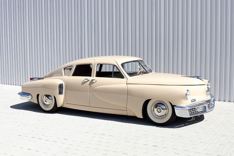 Beige vintage Cadillac sedan parked on a bright lot beside a corrugated metal wall