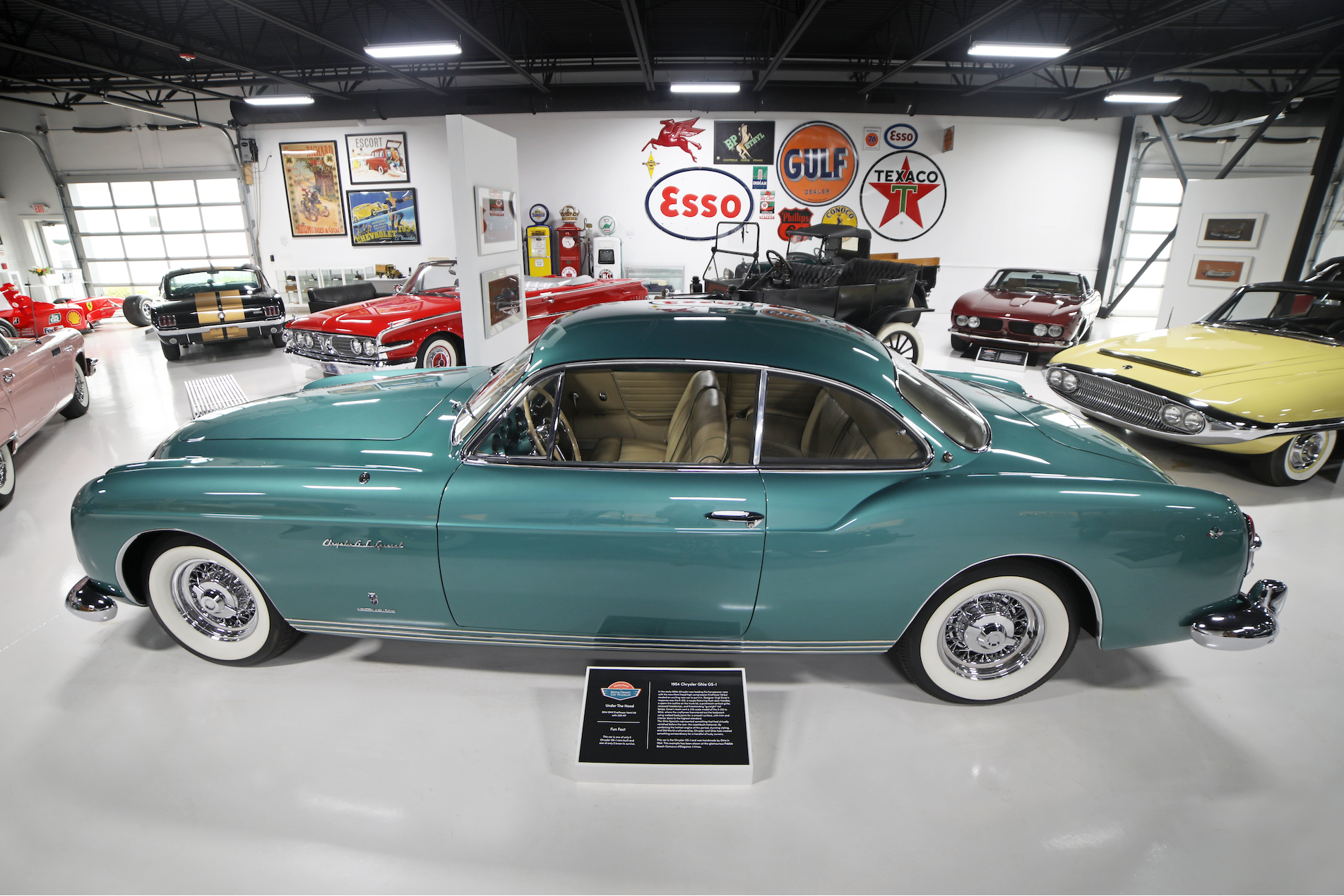 Teal vintage convertible in a classic car showroom with other colorful classic cars and Esso signs