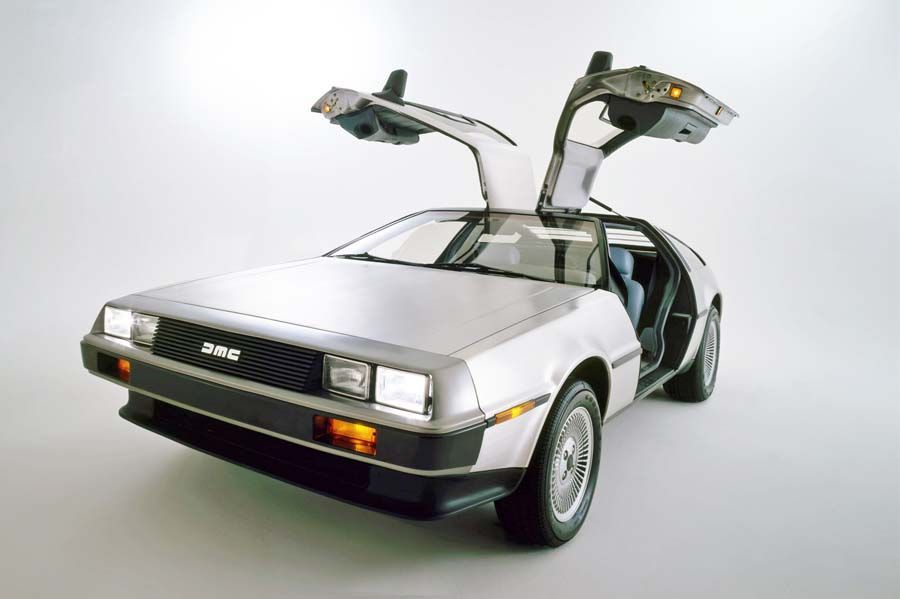 Silver DeLorean sports car with gull-wing doors open, shown in a studio setting