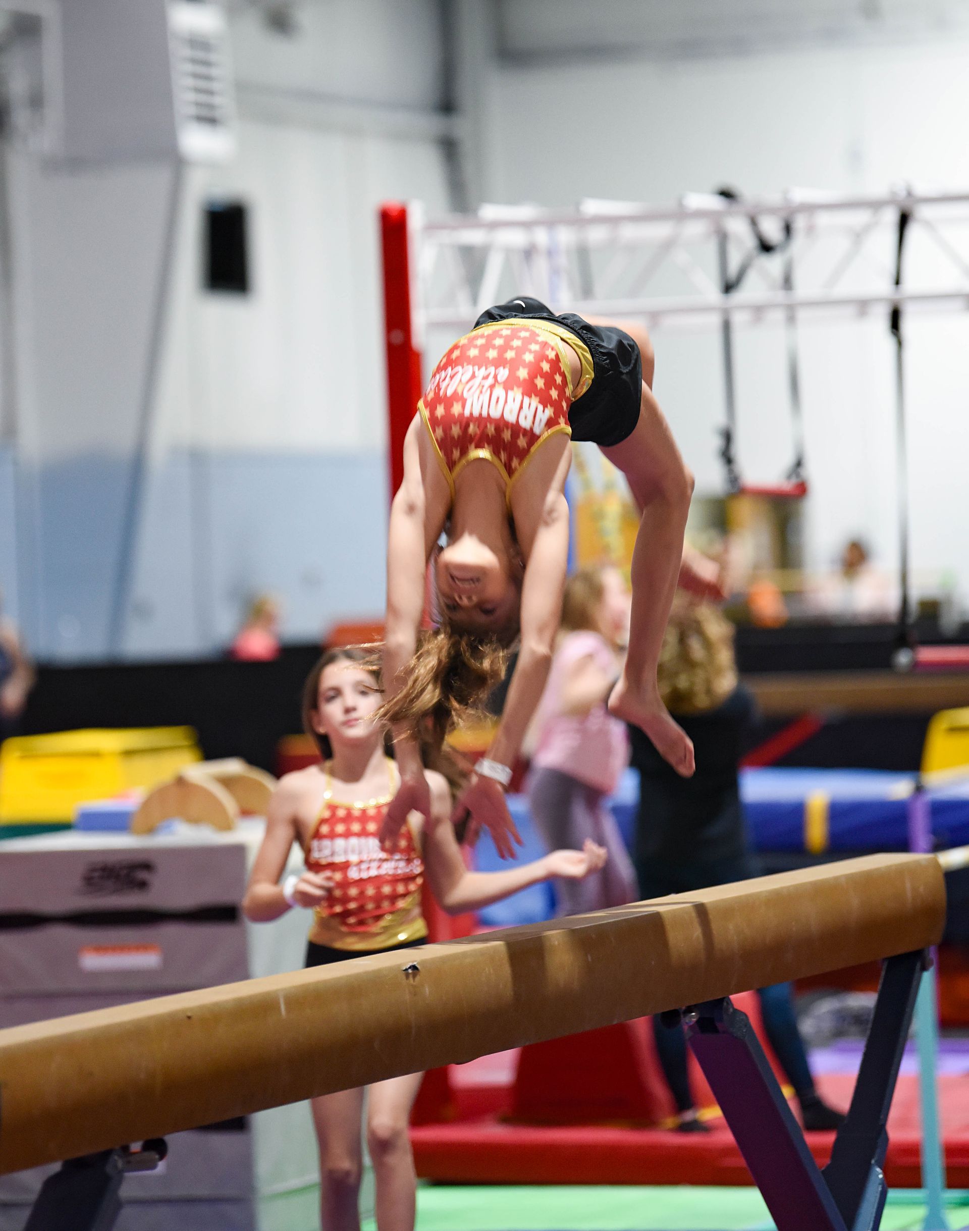 A girl is doing a trick on a balance beam in a gym