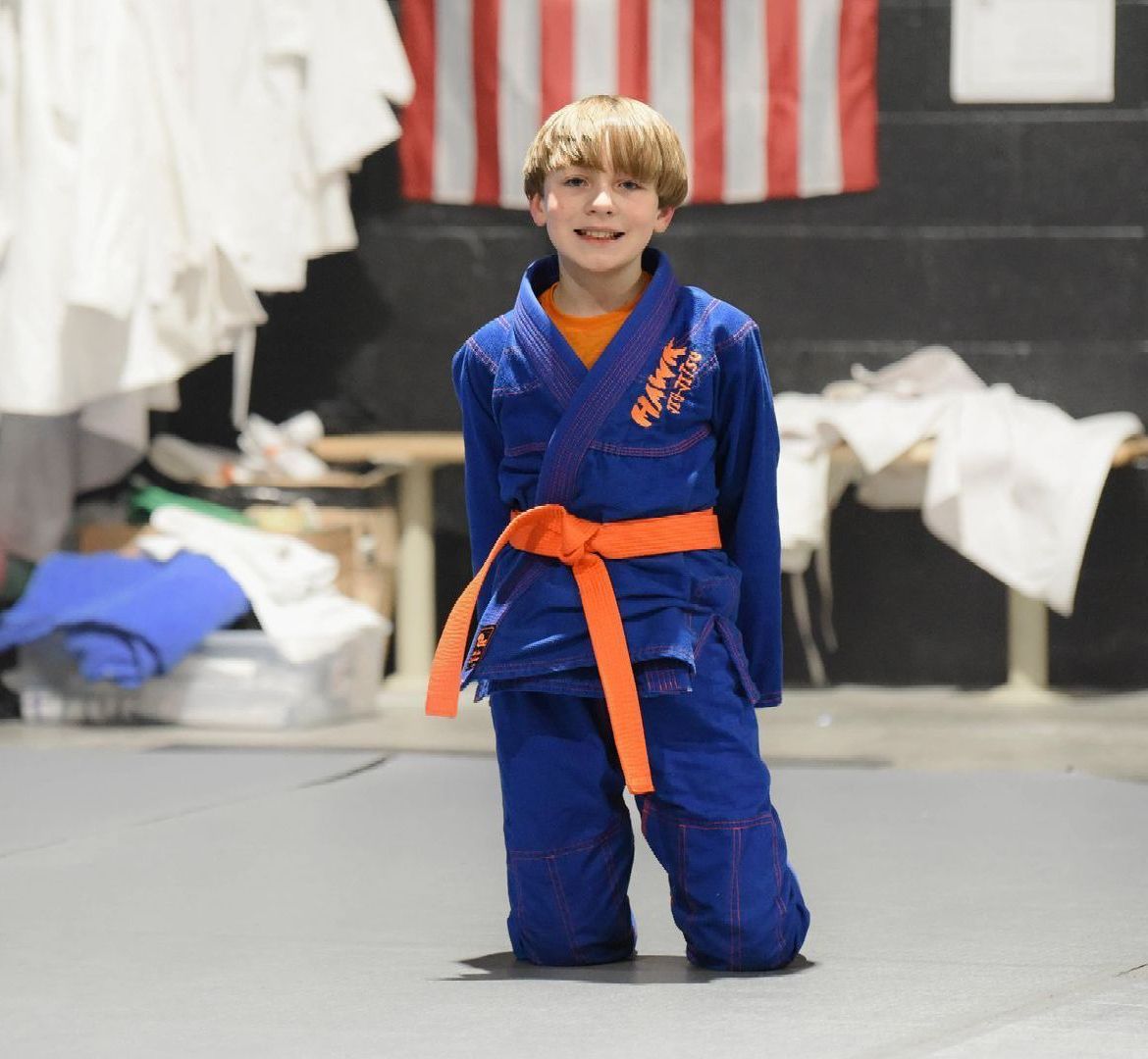 A young boy wearing a blue karate uniform with an orange belt