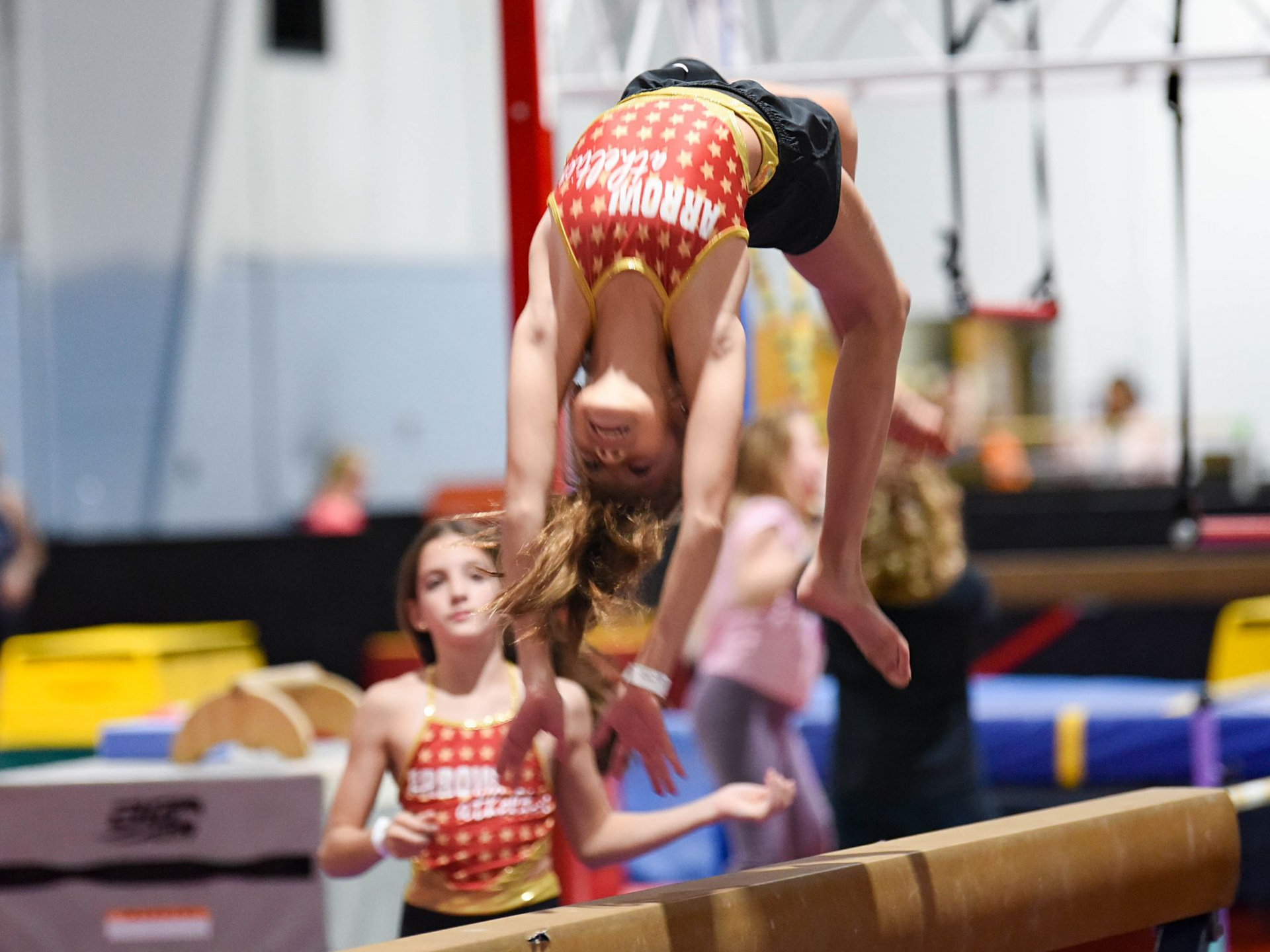 A young girl is doing a handstand on a balance beam in a gym.