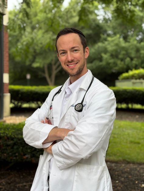 Smiling person in a white shirt outdoors with blurred trees and hills in the background