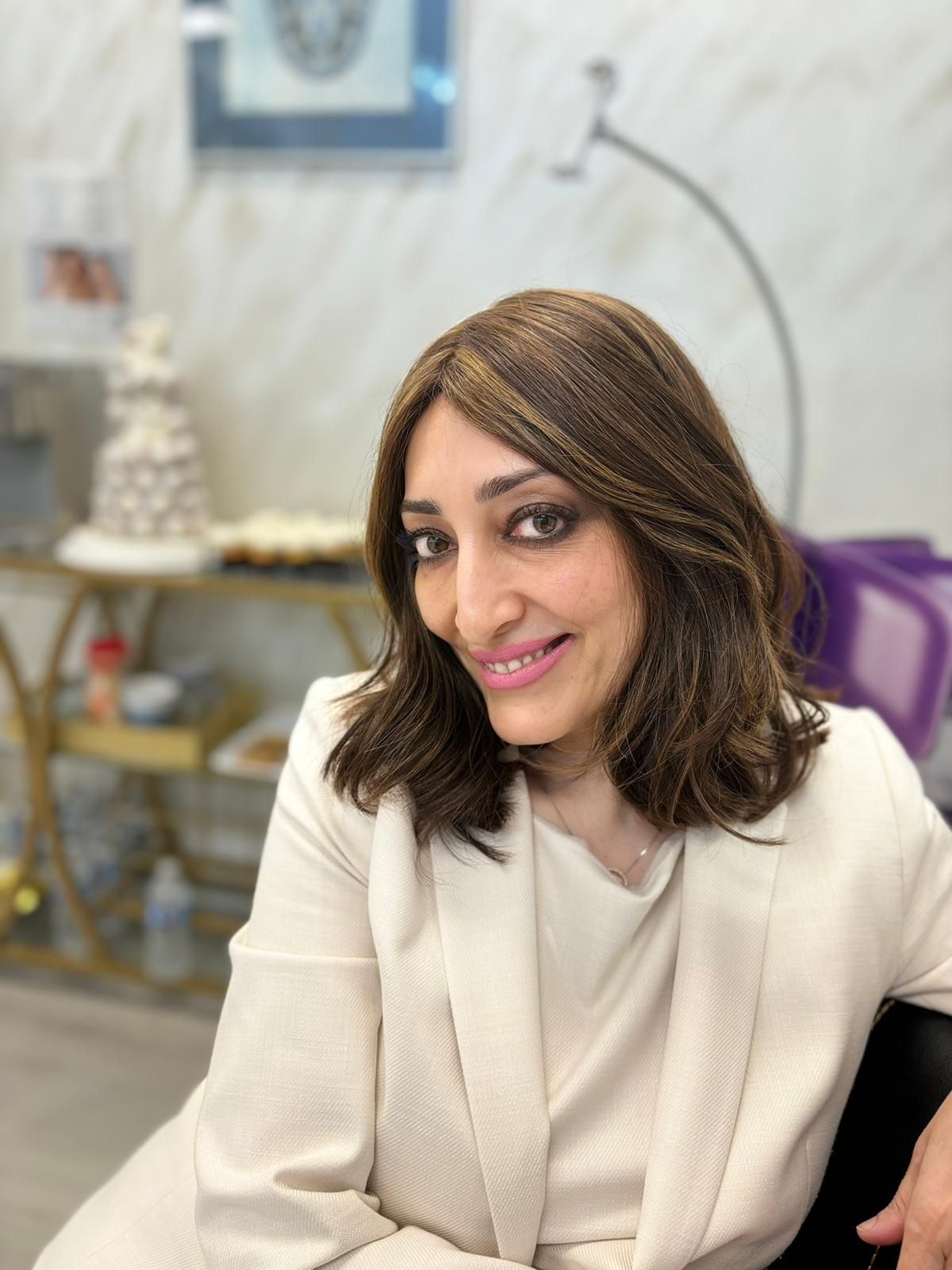 Smiling woman in a cream outfit seated indoors, with a softly blurred home decor background