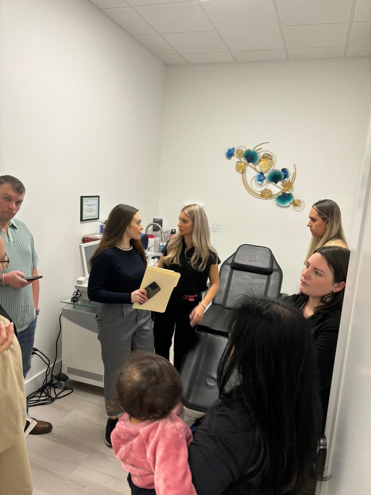 People standing in a small white office, talking near a medical exam chair.