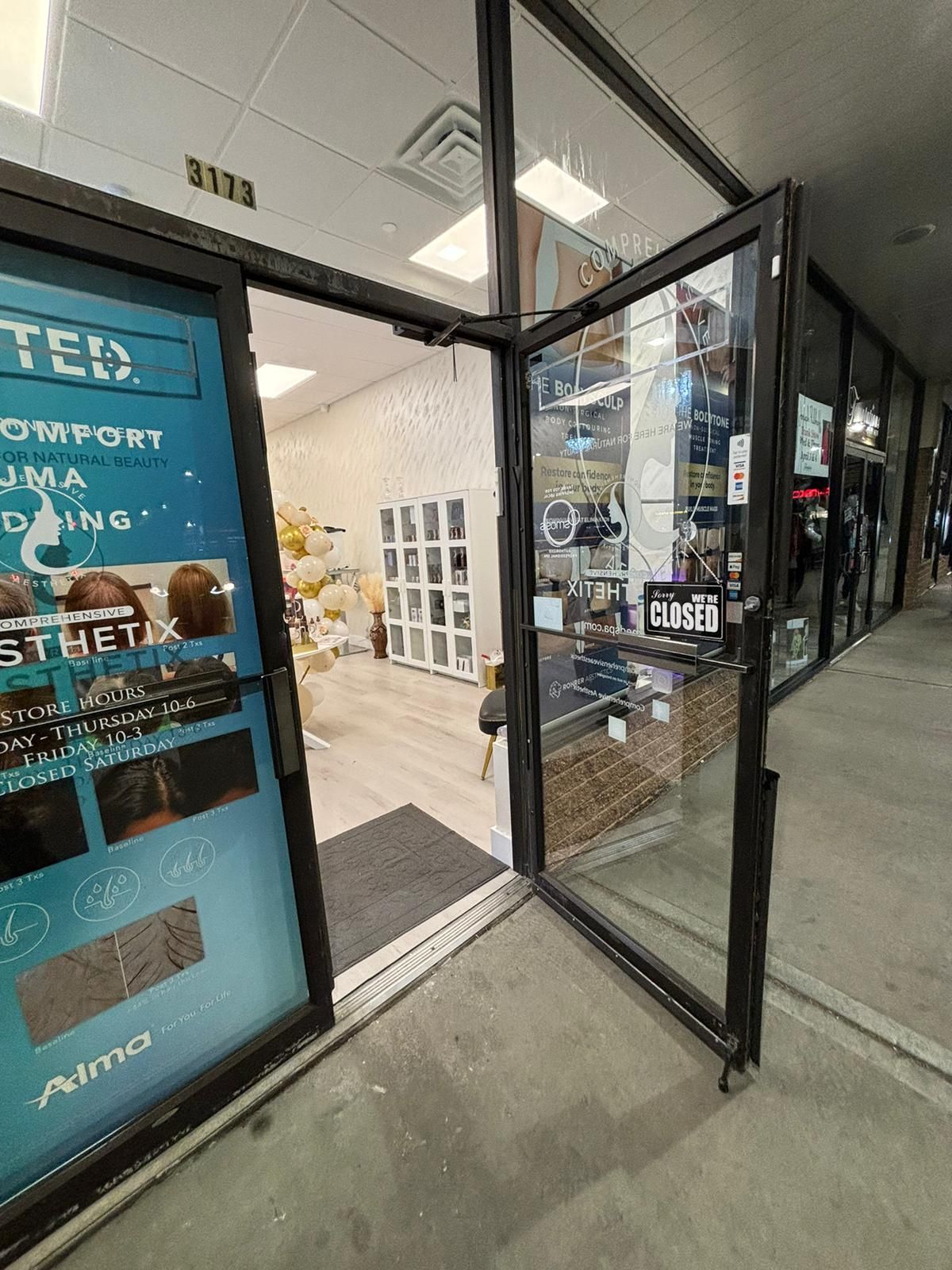 Open glass storefront doorway with blue sale posters and a tiled sidewalk outside.