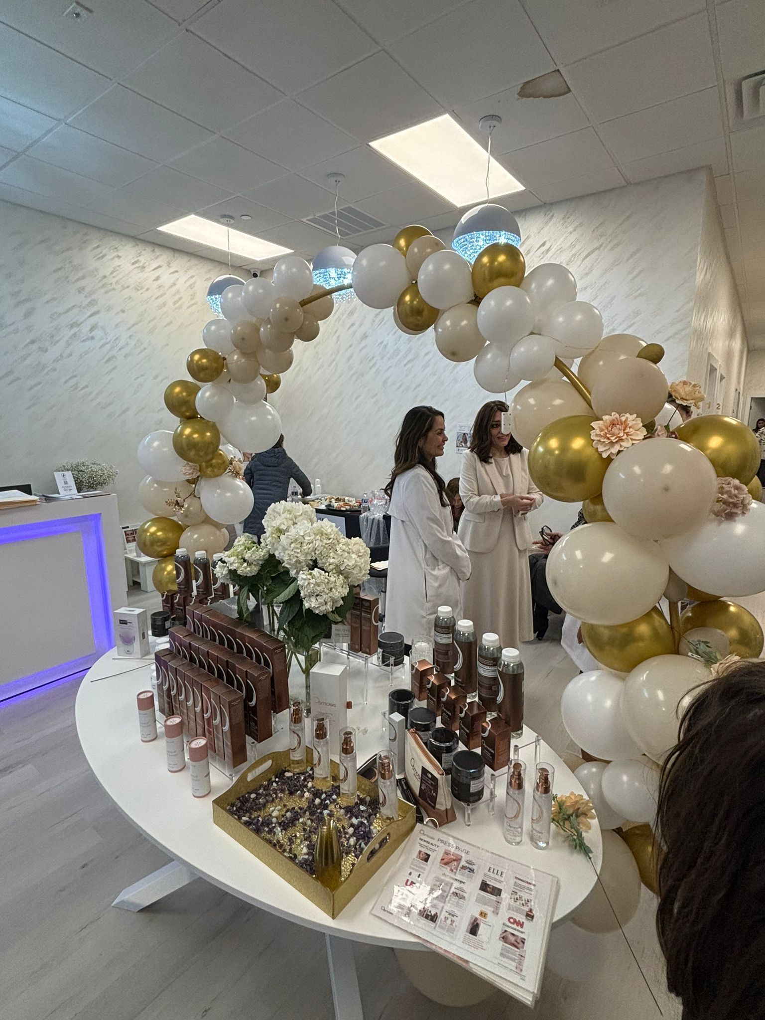 Balloon-decorated display table with products and two people in a bright indoor event space