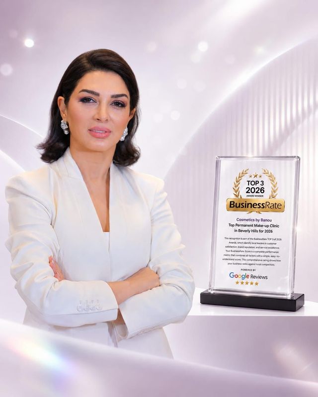 Woman in white stands beside an award plaque on a soft pink background
