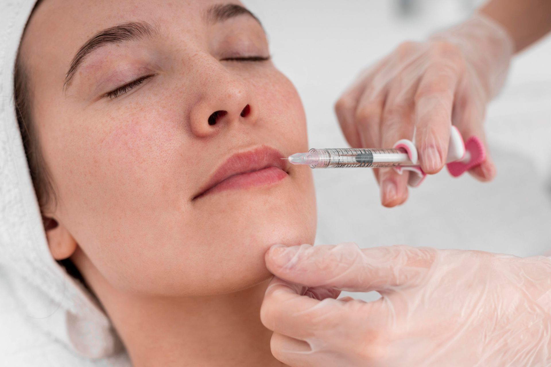 Aesthetician injecting filler into a woman’s lips with a syringe during a cosmetic procedure