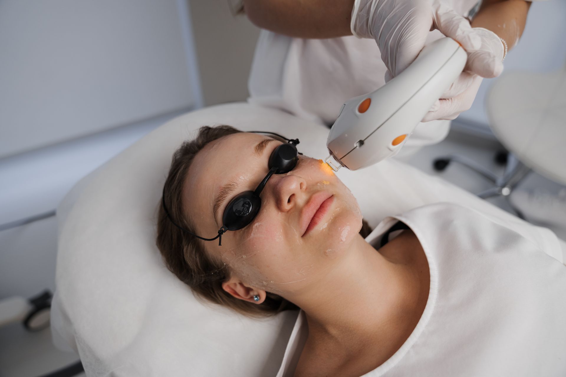 Person wearing protective eyewear receiving a facial laser treatment in a clinic