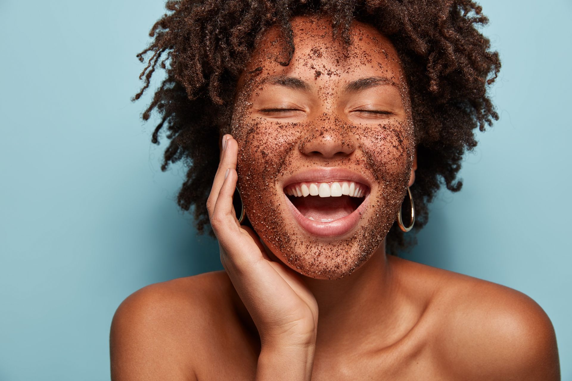 Smiling person with eyes closed touching their face against a blue background
