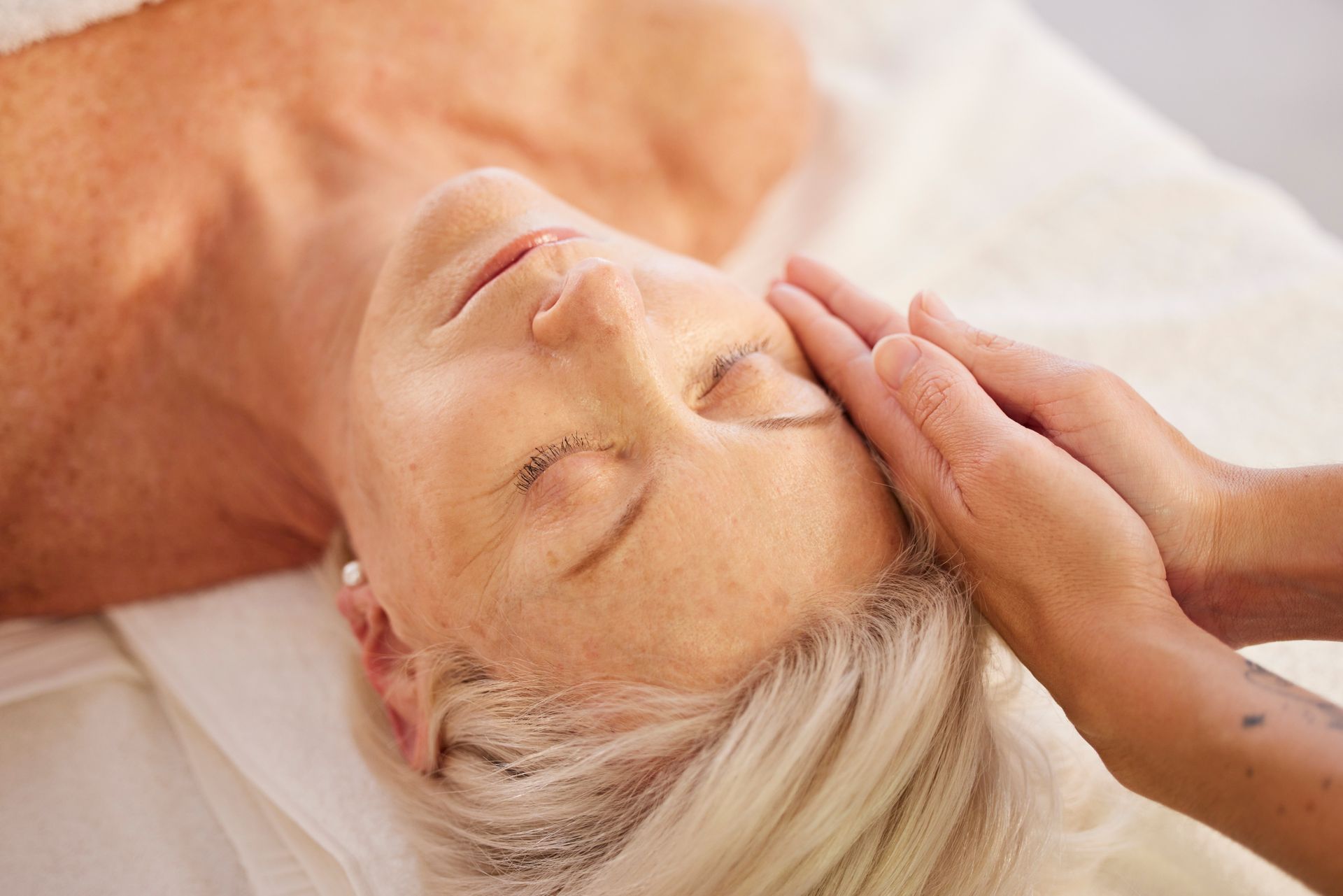 A person receives a gentle facial massage from a practitioner while lying on a treatment table.