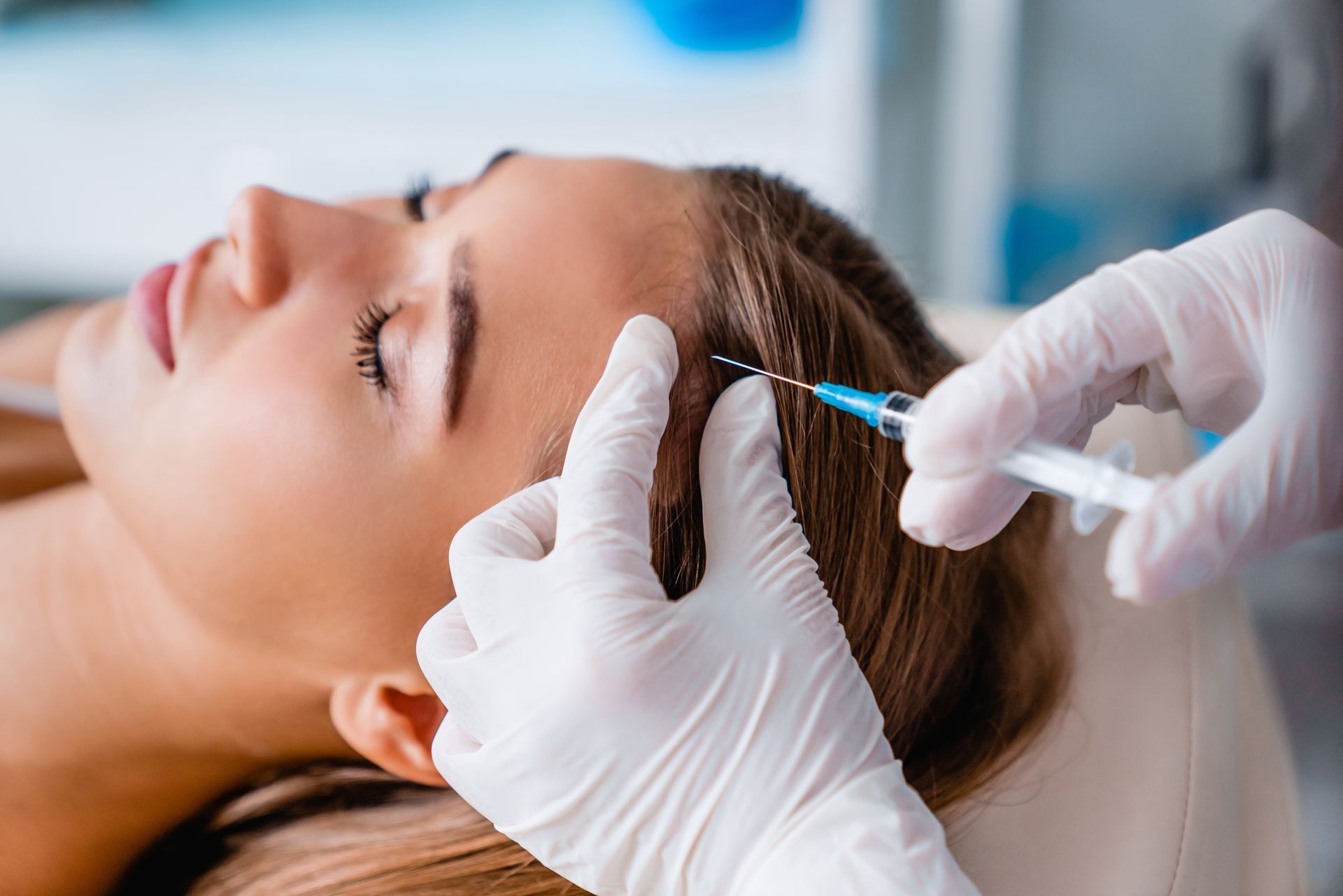 Person receiving a hair injection; gloved hand holding syringe near scalp.