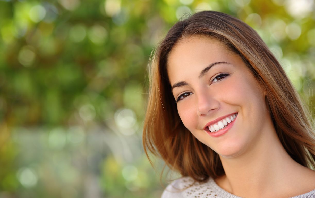A close up of a woman smiling with trees in the background.