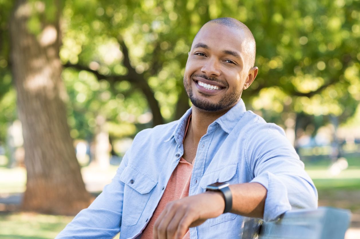 A man is sitting on a bench in a park and smiling.