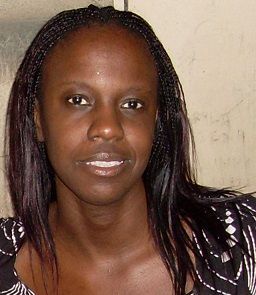Woman with dark skin and braided hair, wearing a patterned top, looking directly at the viewer.