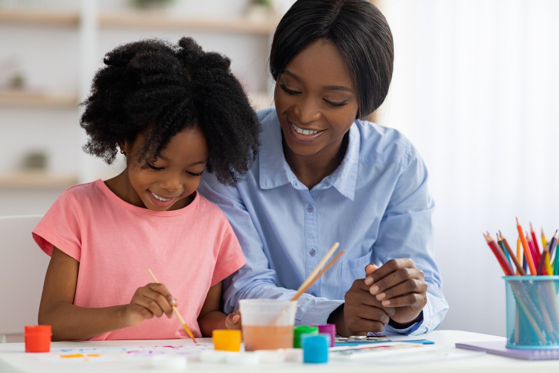Woman and child painting together at a table, smiling.