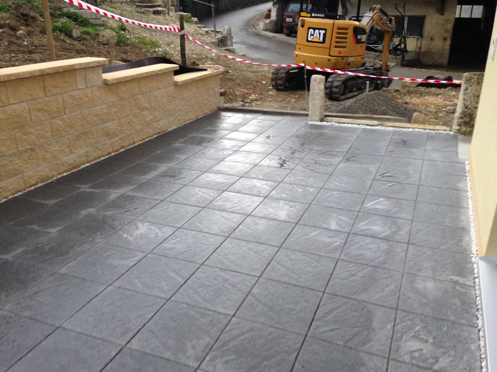 Terrasse carrelée jouxtant un chantier de construction, avec une pelleteuse jaune et du ruban de signalisation rouge